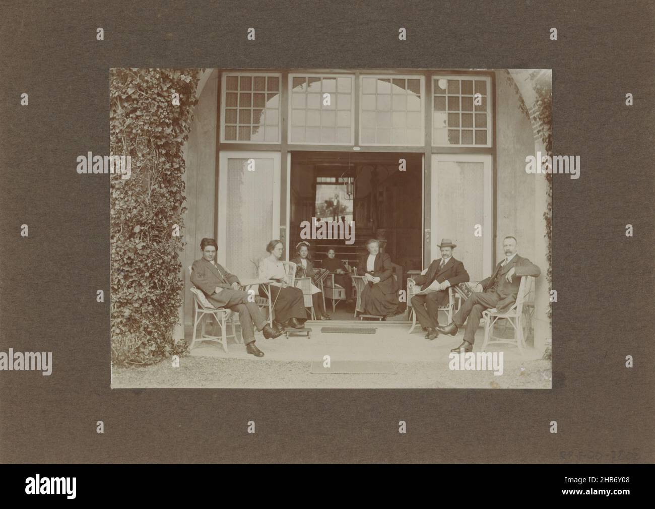 Männer, Frauen und Kinder posieren bei der Veranda, im Hintergrund ist der Fotograf im Spiegel sichtbar, anonym, c. 1900 - c. 1920, Karton, Papier, Höhe 117 mm × Breite 161 mm Stockfoto