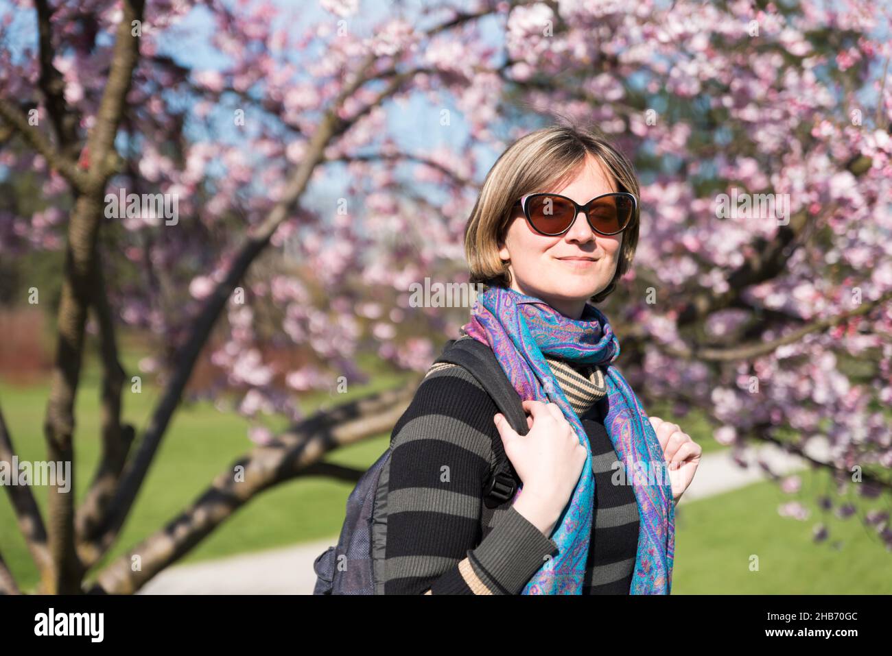 Porträt einer weiblichen Touristen, weiß und 30 Jahre alt, posiert unter den Blüten eines Kirschbaums Stockfoto