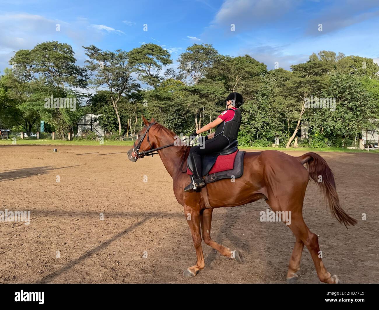 Ein Kind, das eine Schutzausrüstung für Reiten trägt und auf einer Ranch ein braunes Pferd reitet Stockfoto