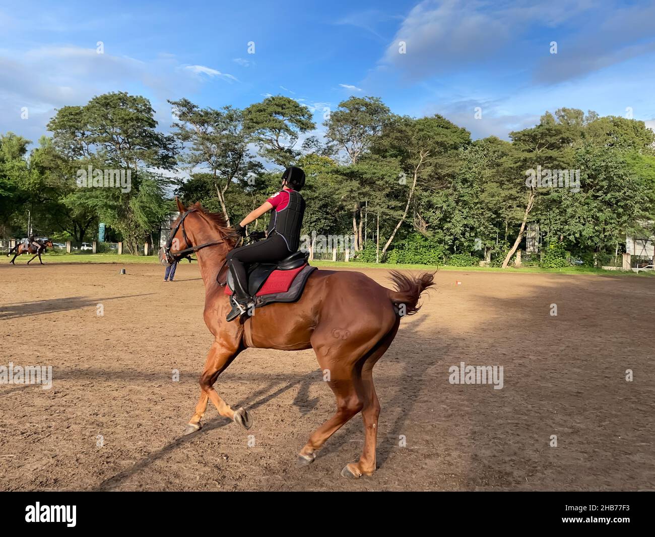 Ein Kind, das eine Schutzausrüstung für Reiten trägt und auf einer Ranch ein braunes Pferd reitet Stockfoto