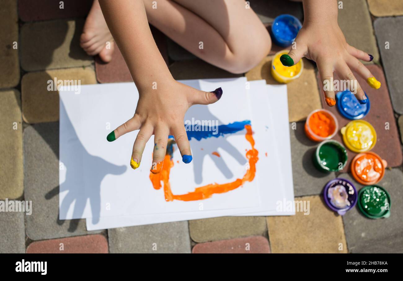 Das Kind zeichnet mit mehrfarbigen Fingerfarben. Die Finger sind mit der Farbe gefärbt. Die Unterhaltung für das Kind, die Entwicklung der kreativen Fähigkeiten bei den Kindern, Stockfoto