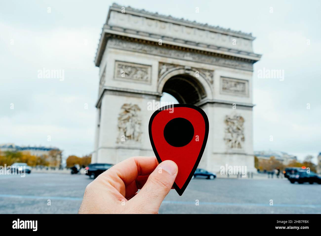 Nahaufnahme der Hand eines jungen kaukasischen Mannes mit einem roten Marker, der auf den Arc de Triomph in Paris zeigt Stockfoto
