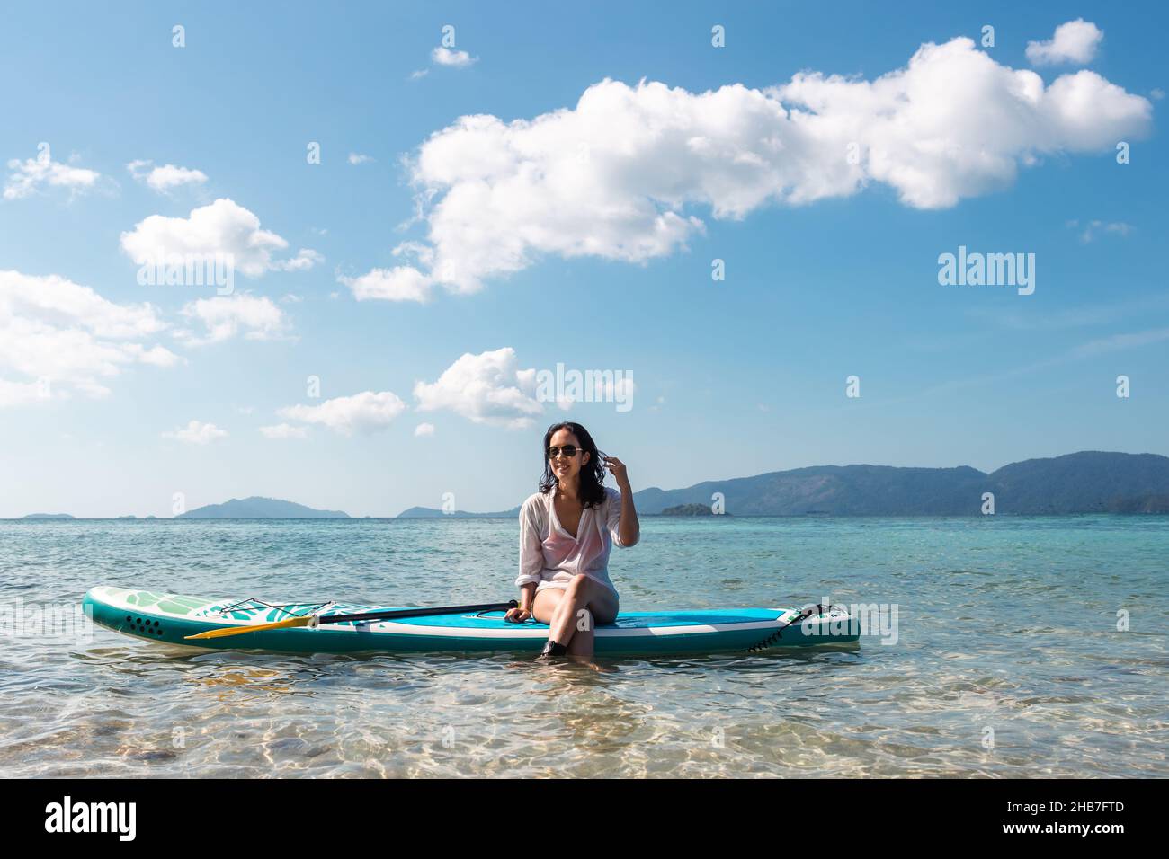 Porträt einer glücklichen Frau mit Sonnenbrille, die an Bord im Meer sitzt. Stockfoto
