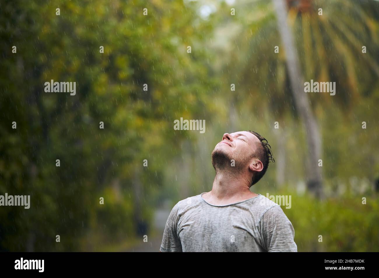 Porträt eines durchnäßten Mannes mit geschlossenen Augen, der starken Regen in der Natur genießt. Stockfoto