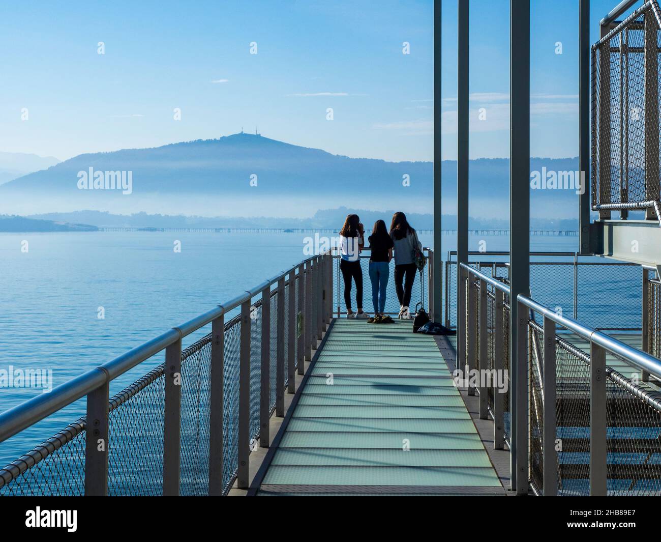 Drei junge Mädchen schauen am Ende eines Laufstegs auf die Bucht von Santander, um sie an einem klaren Tag zu beobachten. Stockfoto