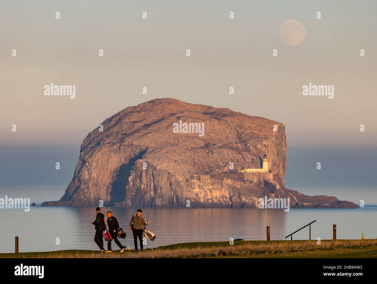 North Berwick, East Lothian, Schottland, Großbritannien, 17th. Dezember 2021. UK Wetter: Vollmond steigt über Bass Rock auf. Der Dezember-Vollmond wird als „Kalte Mond“ bezeichnet. Heute stieg es kurz vor Sonnenuntergang. Im Bild: Golfer genießen ein letztes Spiel, bevor die Sonne auf dem Golfplatz Glen untergeht Stockfoto