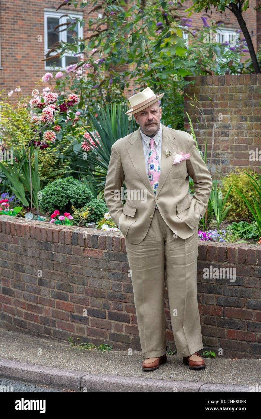 Ein Mann im Sommeranzug und Hut, der vor Blumen steht Stockfoto