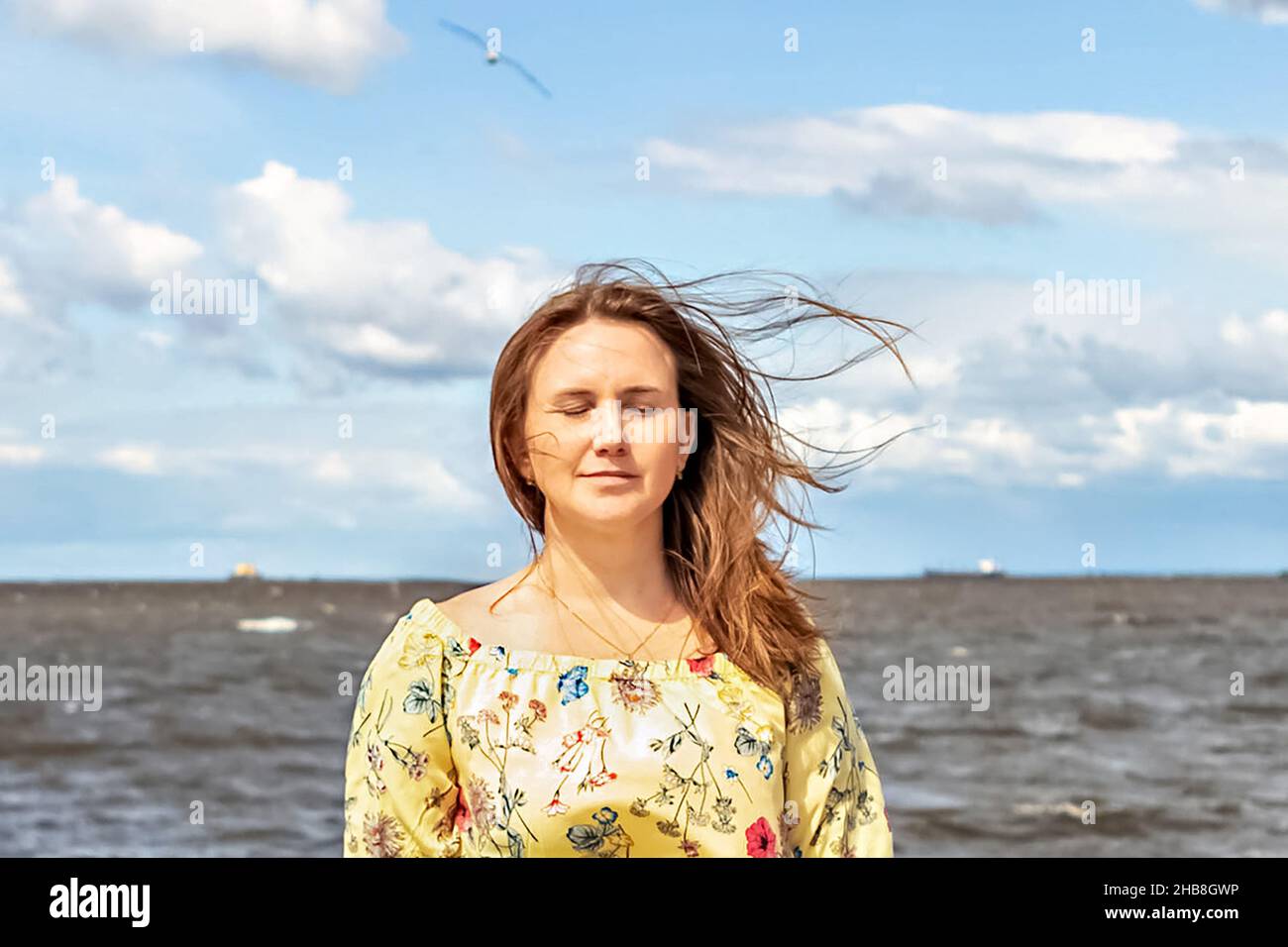 Ein großes Porträt einer jungen Frau mit flatternden Haaren im Wind an der Küste. Stockfoto