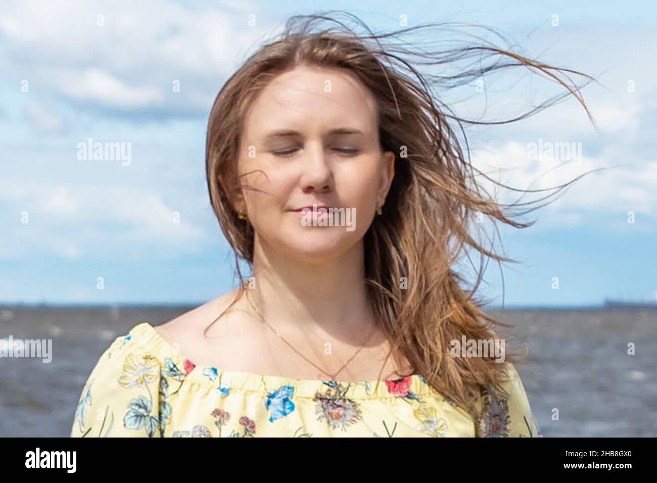 Ein großes Porträt einer jungen Frau mit flatternden Haaren im Wind an der Küste. Stockfoto