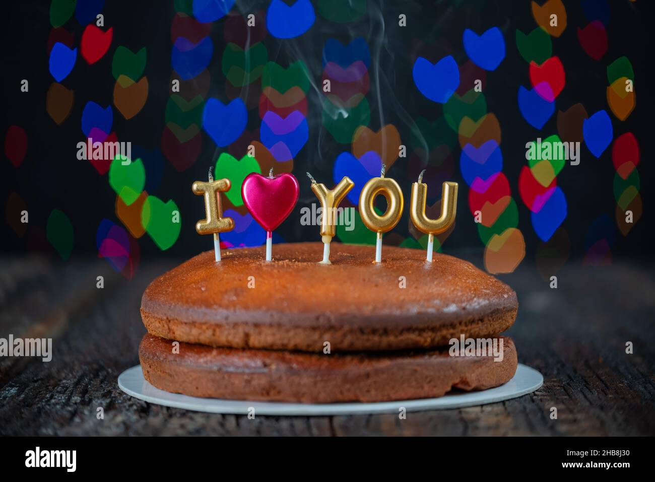 Schichten eines Kuchens mit I love you Kerzen, ein Herz auf einem Vintage-Tisch und bunte Bokeh-Muster im Hintergrund. Romantisches Konzept. Stockfoto