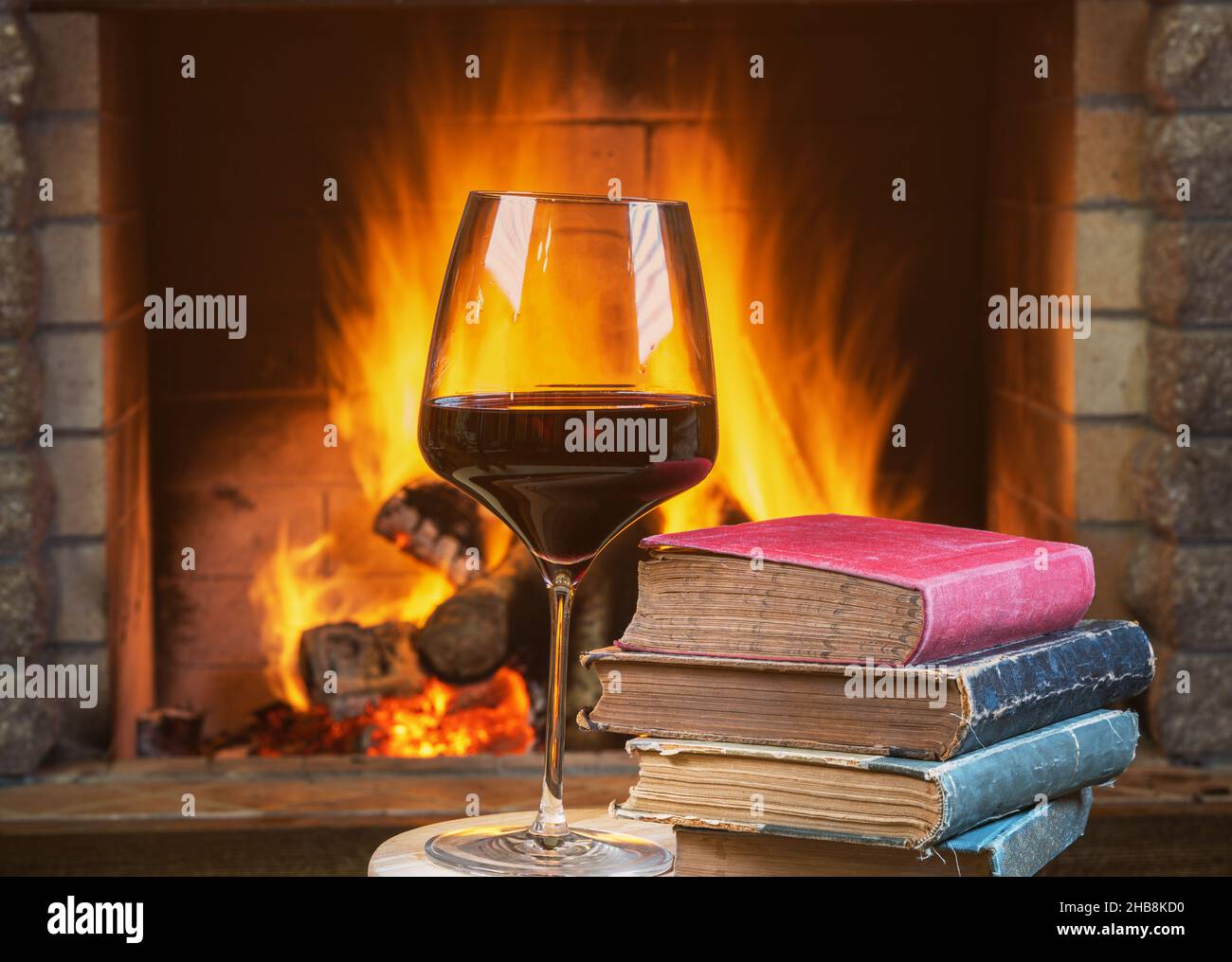 Ein Glas Rotwein und alte Bücher in der Nähe eines gemütlichen Kamins, . Stockfoto