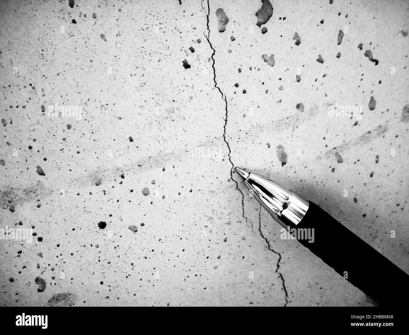 Flacher Haarriss in frischem Beton durch Schrumpfung während des Aushärtens. Als Referenz verwendeter Stift. Stockfoto