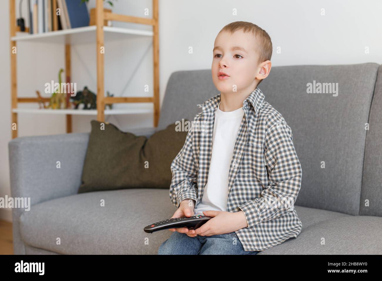 Kind mit Fernbedienung. Junge ohne elterliche Kontrolle beim Fernsehen. Frühkindliche Bildung und Freizeit im Elementaralter. Stockfoto