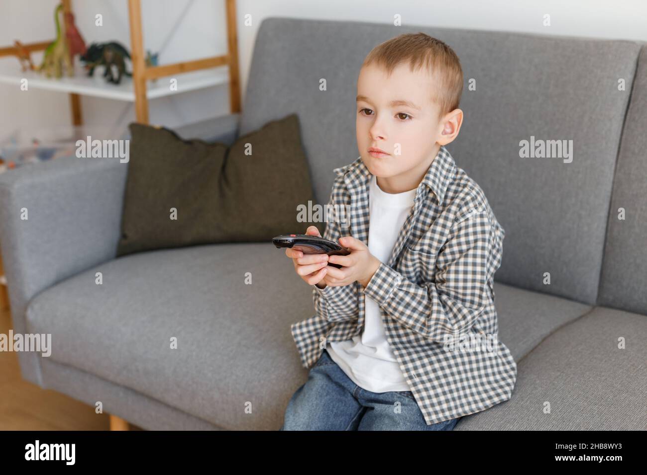 Kind mit Fernbedienung. Junge ohne elterliche Kontrolle beim Fernsehen. Frühkindliche Bildung und Freizeit im Elementaralter. Stockfoto