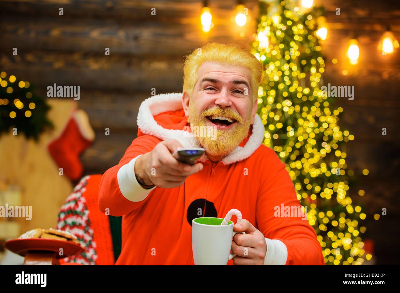 Glücklicher Weihnachtsmann mit Heißgetränk beim Anschauen des Weihnachtsfilms. Unterhaltung und Kino. Hintergrund zum neuen Jahr Stockfoto