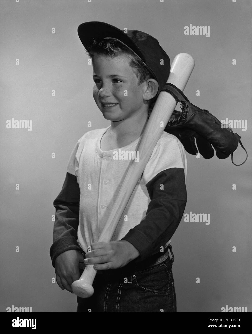 Junge in langärmeligen Baseballhemd und Baseballhut, der zur Seite schaut,  mit dem Schläger, der über seine Schulter gestrickter Schläger, mit dem  Handschuh, der am Schläger angehängt ist. 1965 Stockfotografie - Alamy