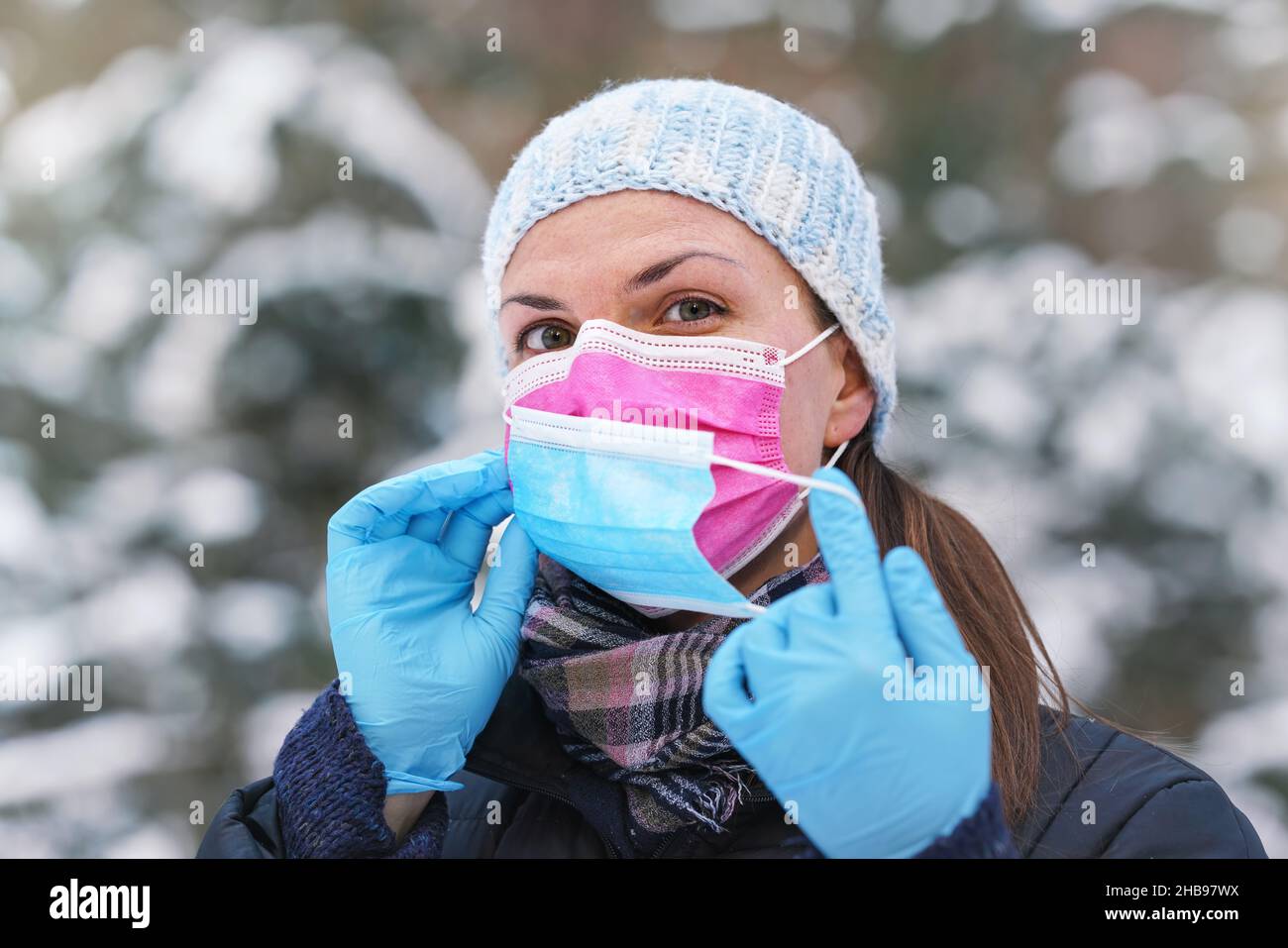 Junge Frau in warmer Winterkleidung trägt rosa Einweg-Virus Gesichtsmaske, setzen eine andere auf - einige raten, dass zwei Schichten bietet bessere Prot Stockfoto