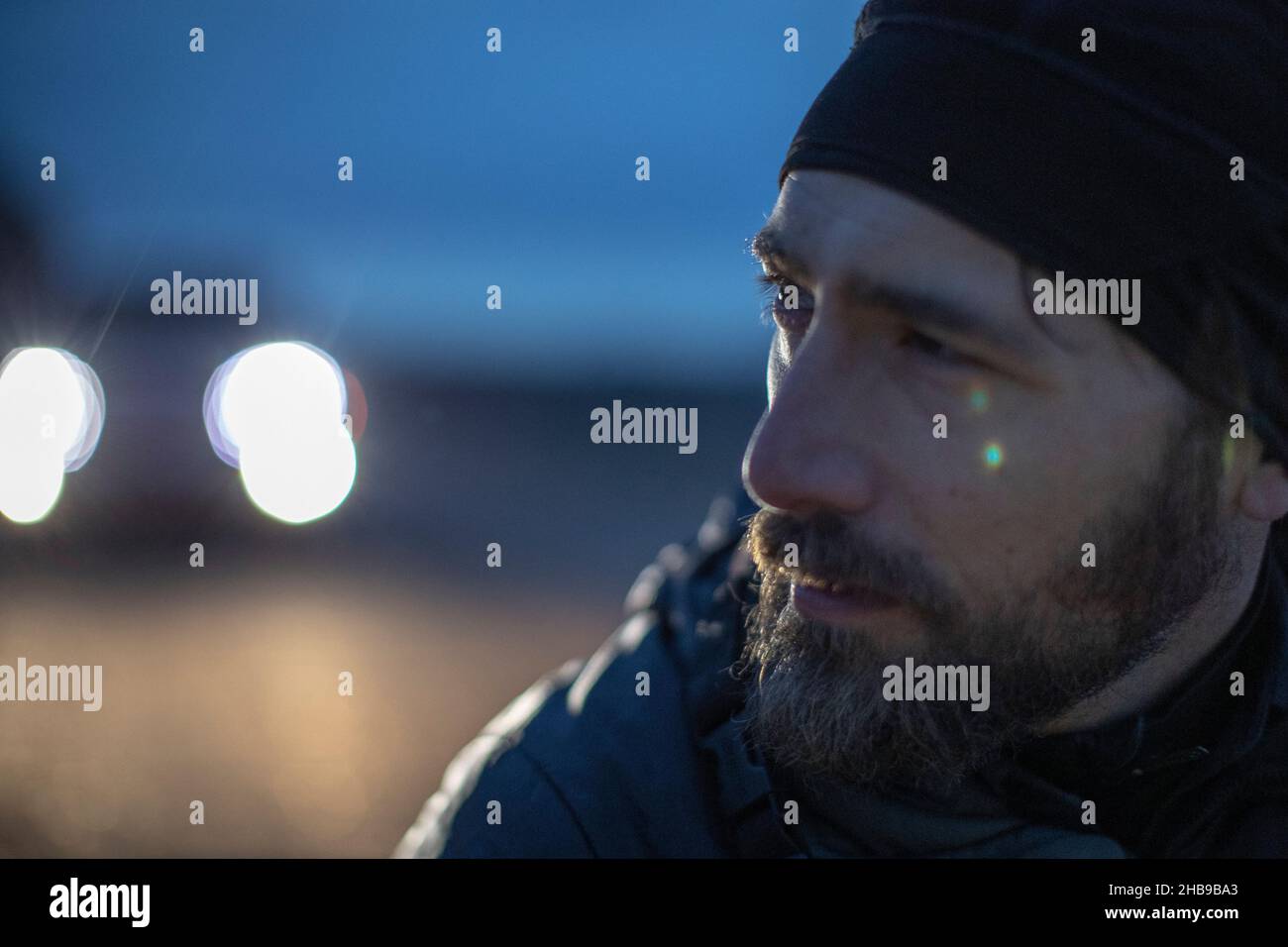 Der Mensch verlor sich in Gedanken, draußen in der Dämmerung mit Autoscheinwerfern im Hintergrund Stockfoto