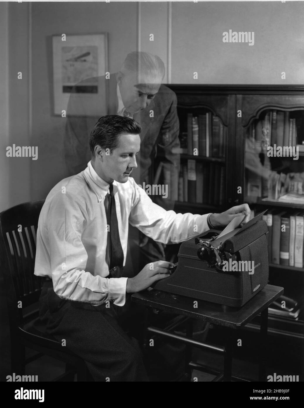 Ein Mann an einer Schreibmaschine, abgebildet mit der Erscheinung eines älteren Mannes an seiner Schulter.circa 1955 Stockfoto