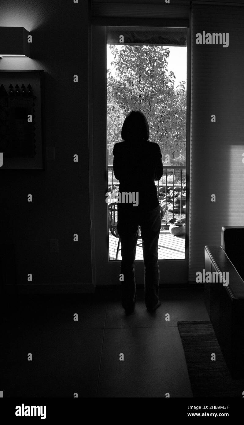 Eine Frau steht an ihrem Backdoo und schaut an einem sonnigen Tag draußen. Stockfoto