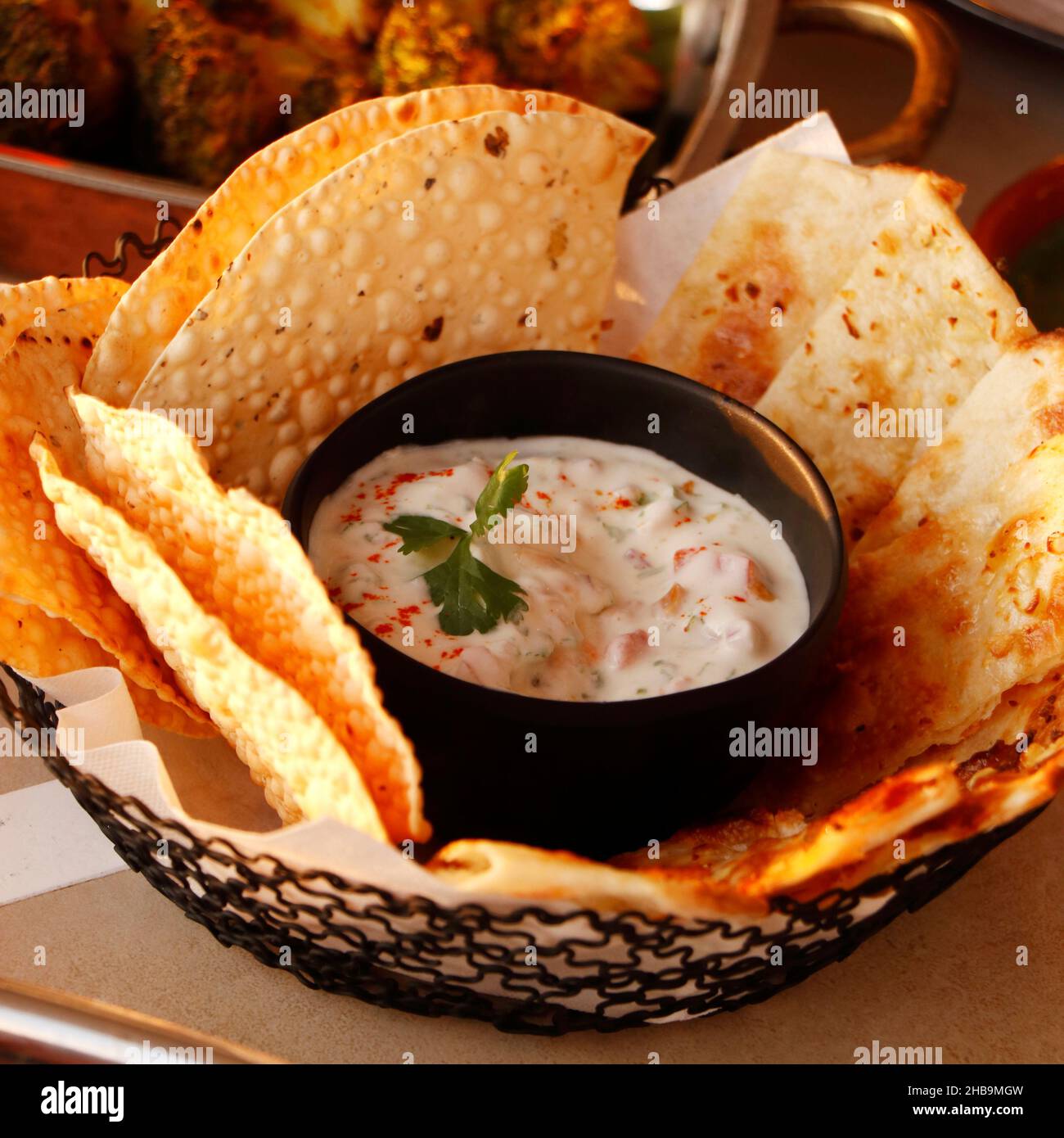 indischer Snack, Masala Papad und knuspriges Naan-Brot in einem Korb mit Joghurt-Raita Stockfoto