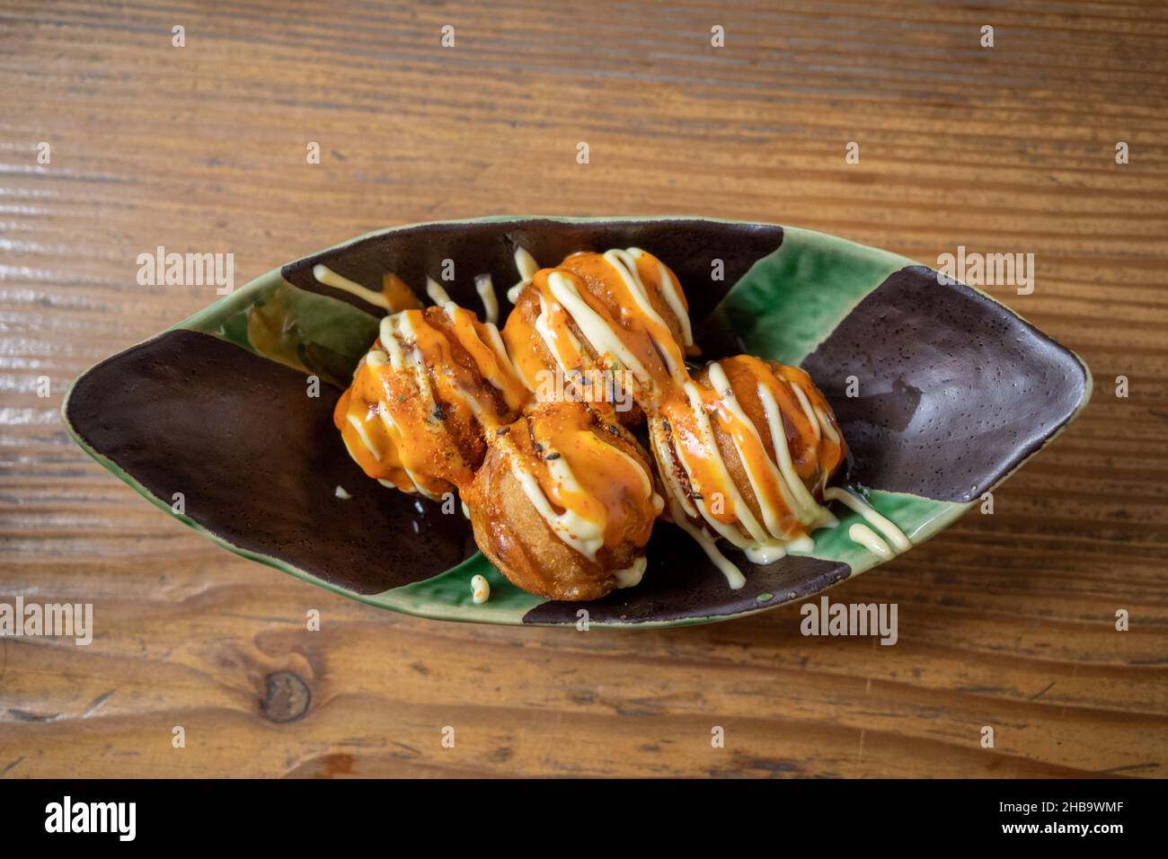 Selektiver Fokus und Draufsicht auf Takoyaki- oder japanische Krake-Kugeln, serviert auf weißem Teller auf Holztheke im japanischen Restaurant. Stockfoto