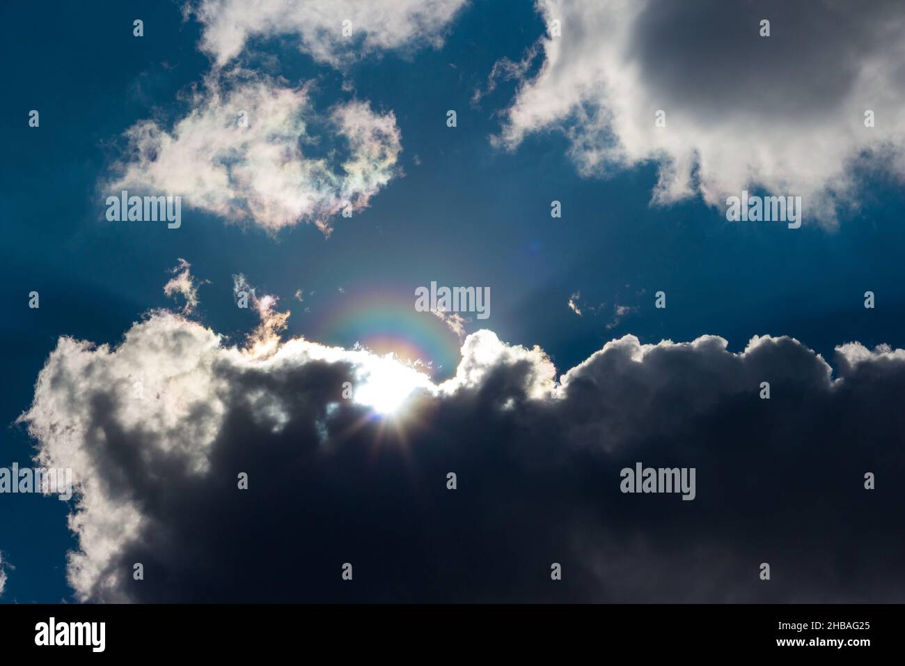 Die Sonne mit einem Regenbogen-Halo guckt hinter den Wolken hervor, teilweise bewölkt am Himmel Stockfoto