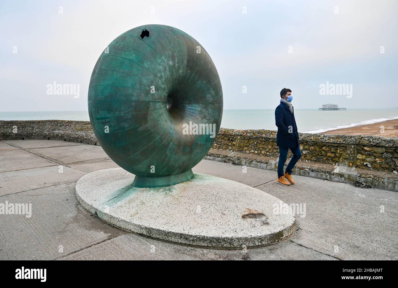 Brighton, Großbritannien. 18th. Dezember 2021 - Ein Besucher an der Küste von Brighton bei der Donut-Skulptur an einem ruhigen, bewölkten Morgen, da das sesshafte Wetter in den nächsten Tagen in Großbritannien anhalten wird : Credit Simon Dack / Alamy Live News Stockfoto
