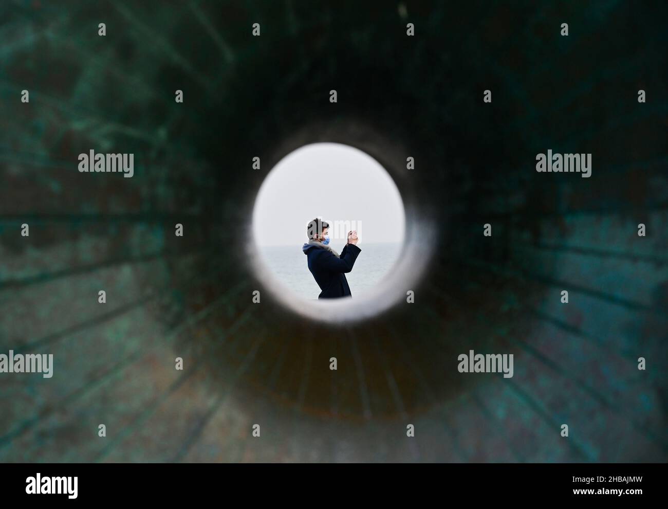 Brighton, Großbritannien. 18th. Dezember 2021 - Ein Besucher an der Küste von Brighton bei der Donut-Skulptur an einem ruhigen, bewölkten Morgen, da das sesshafte Wetter in den nächsten Tagen in Großbritannien anhalten wird : Credit Simon Dack / Alamy Live News Stockfoto