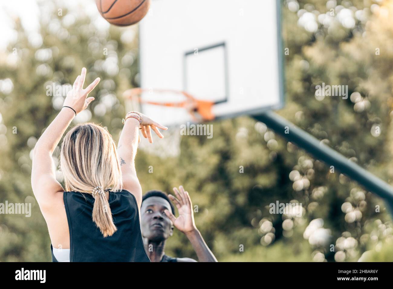 Selektiver Fokus auf eine Frau, die einen Ball auf den Korb schießt, während ein Mann ihn verteidigt Stockfoto