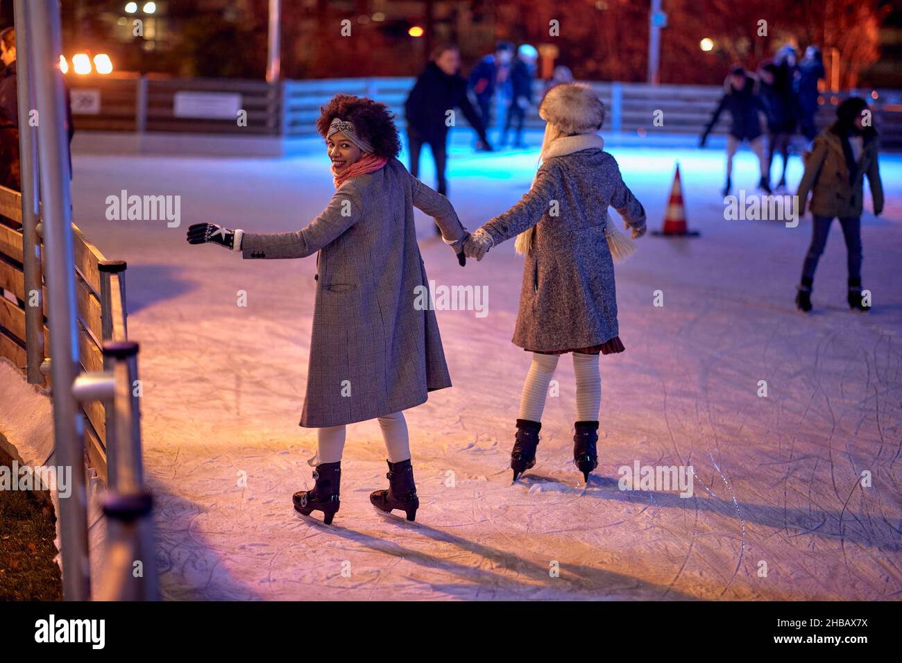 Eine Aufnahme von zwei Freundinnen aus dem Rücken, während sie während der Weihnachtsferien auf der Eislaufbahn in einer schönen Nacht in der Stadt Schlittschuhlaufen. Weihnachten, N Stockfoto