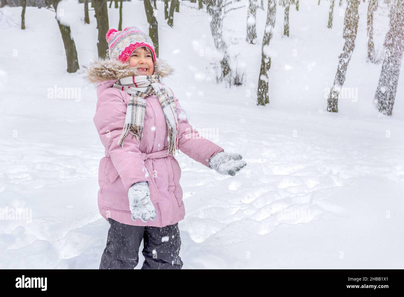 Ein glückliches zahnloses kleines Mädchen, das im Wald mit Schnee spielt. Stockfoto