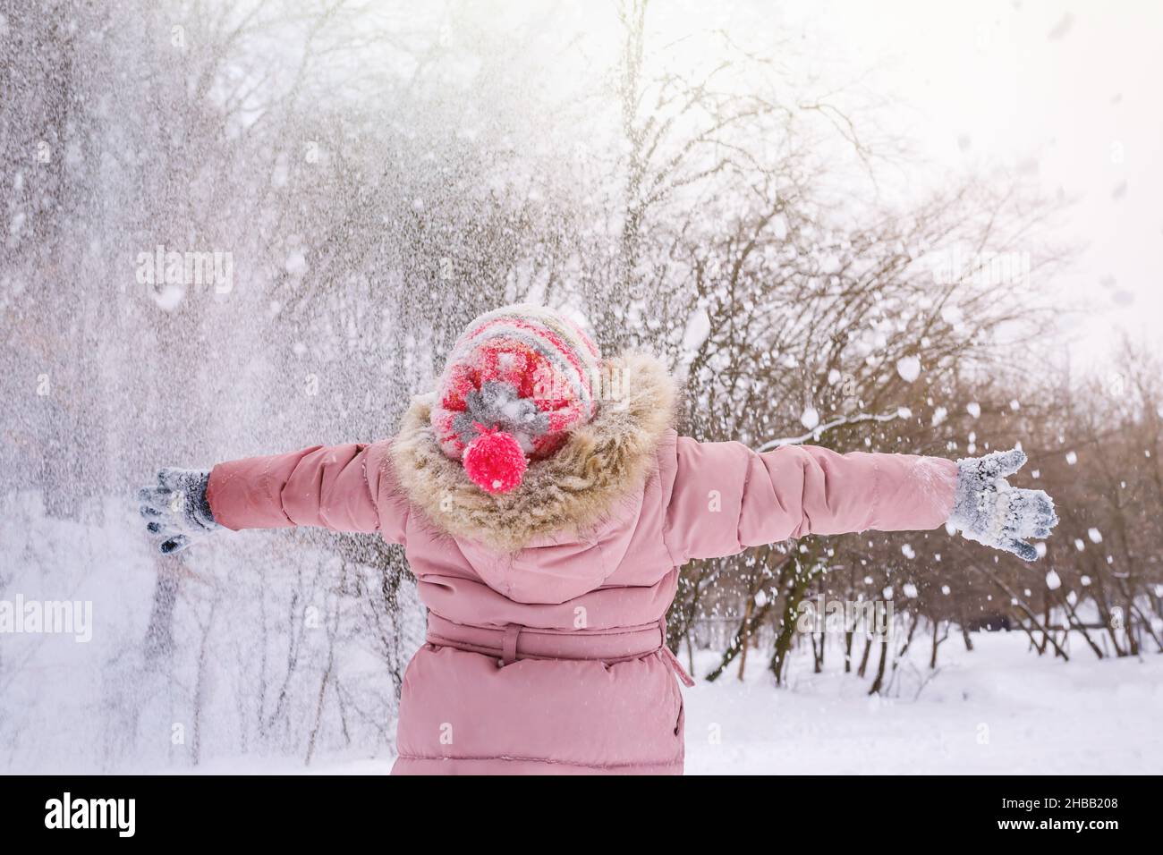 Ein glückliches kleines Mädchen, das im Wald mit Schnee spielt. Blick von hinten. Stockfoto