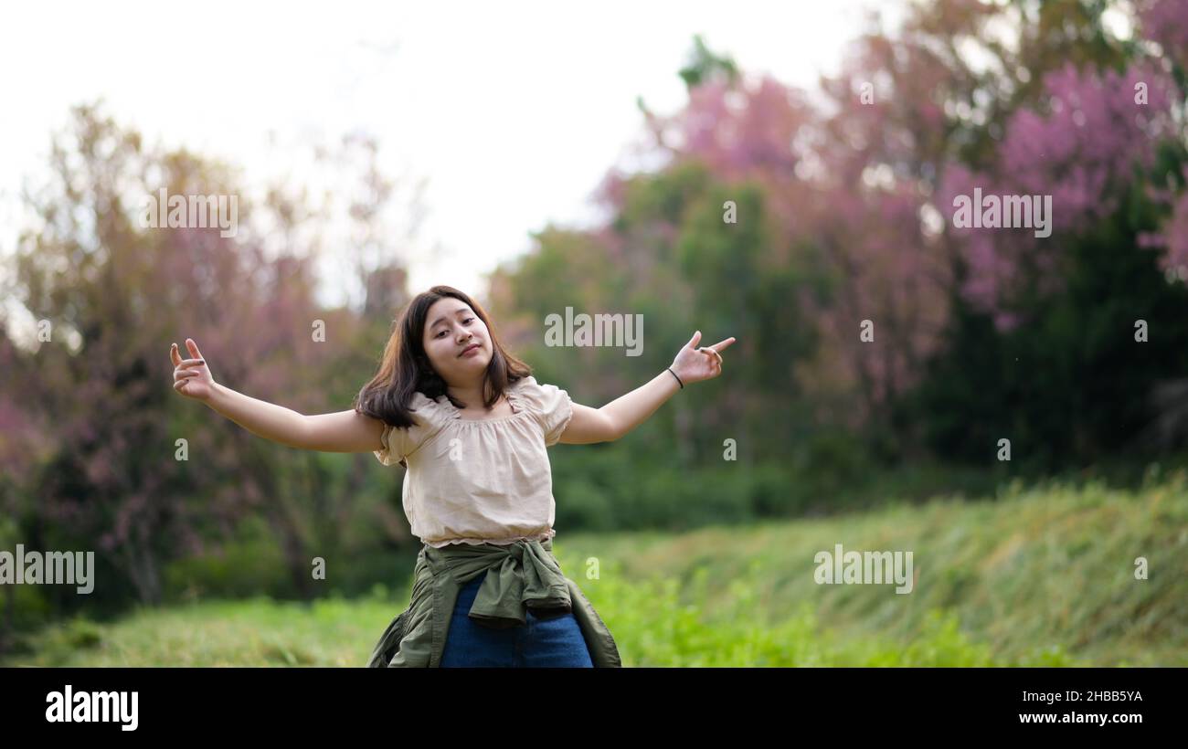 Das asiatische Mädchen lächelt verschmitzt und wendet sich während einer Naturtour der Kamera zu, sie spreizte beide Arme. Stockfoto