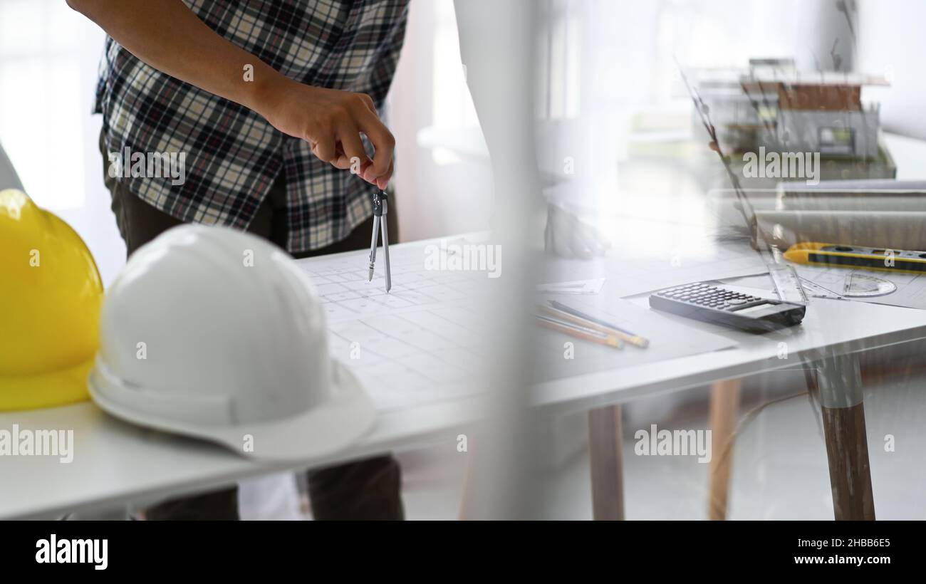 Designer verwenden Kompasse, um Entwürfe auf Häuserpläne, Hauspläne und Schutzhelme mit Zeichenwerkzeugen auf den Tisch zu zeichnen. Stockfoto