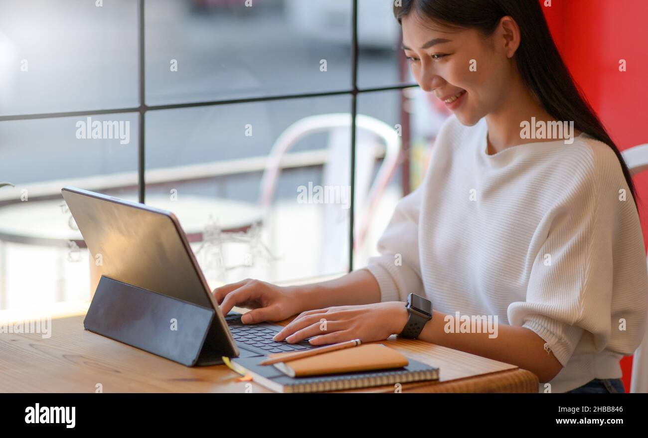 Eine junge Frau betreibt in einem Café einen Laptop mit lächelndem Ausdruck. Stockfoto