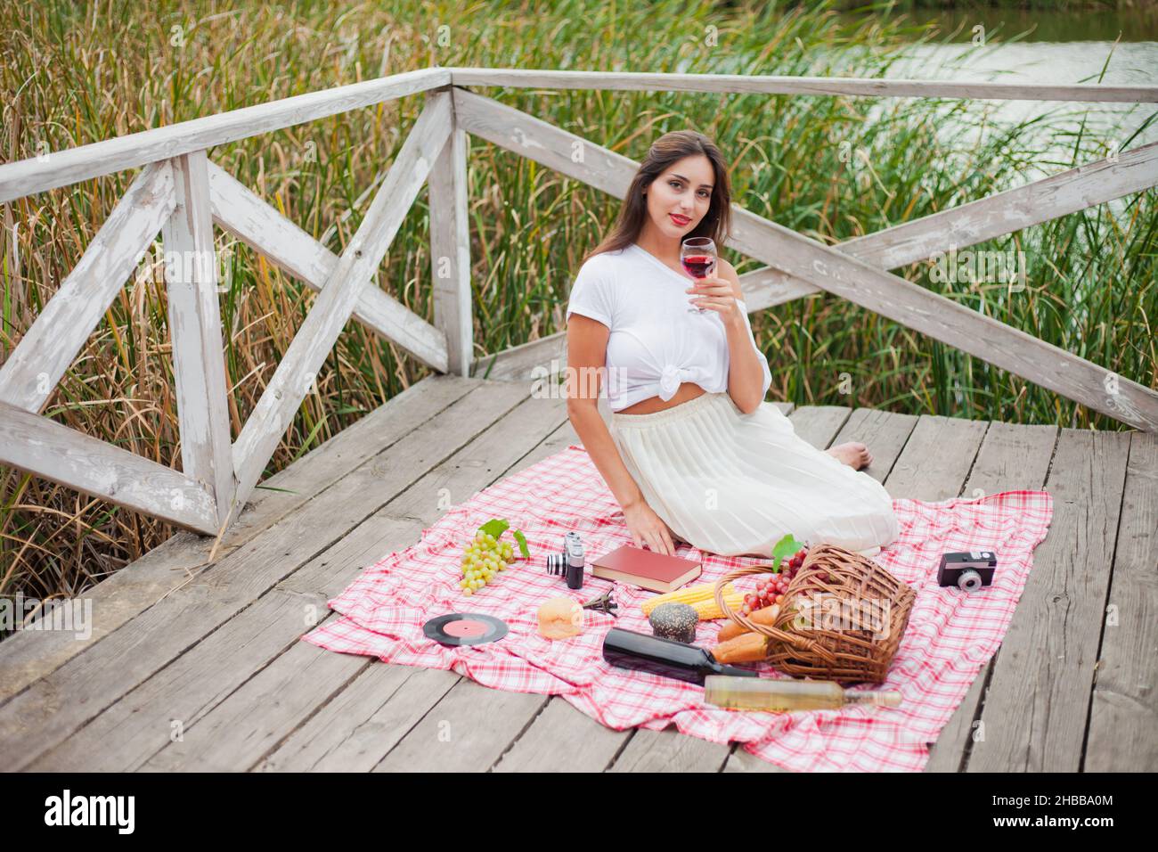 Schöne junge Frau in Vintage-Retro-Kleidung hat Picknick auf hölzernen Pier allein. Picknick im Freien im französischen Stil Stockfoto