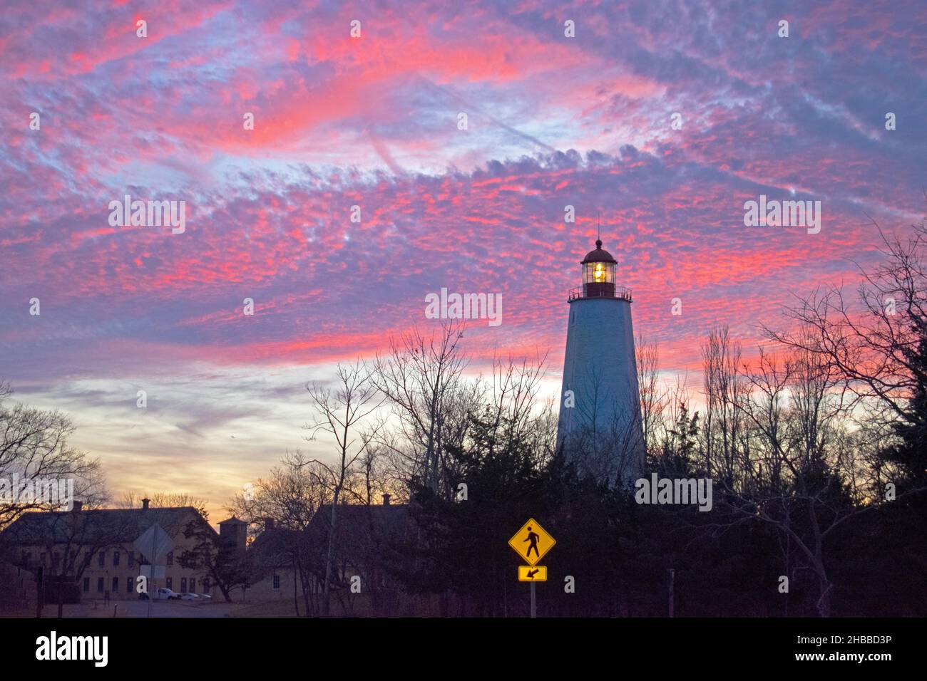 Leuchtturm in Sandy Hook, New Jersey, in der Dämmerung, mit seinem hellen Licht, das auf einem bunt bewölkten Sonnenuntergangshintergrund -54 scheint Stockfoto