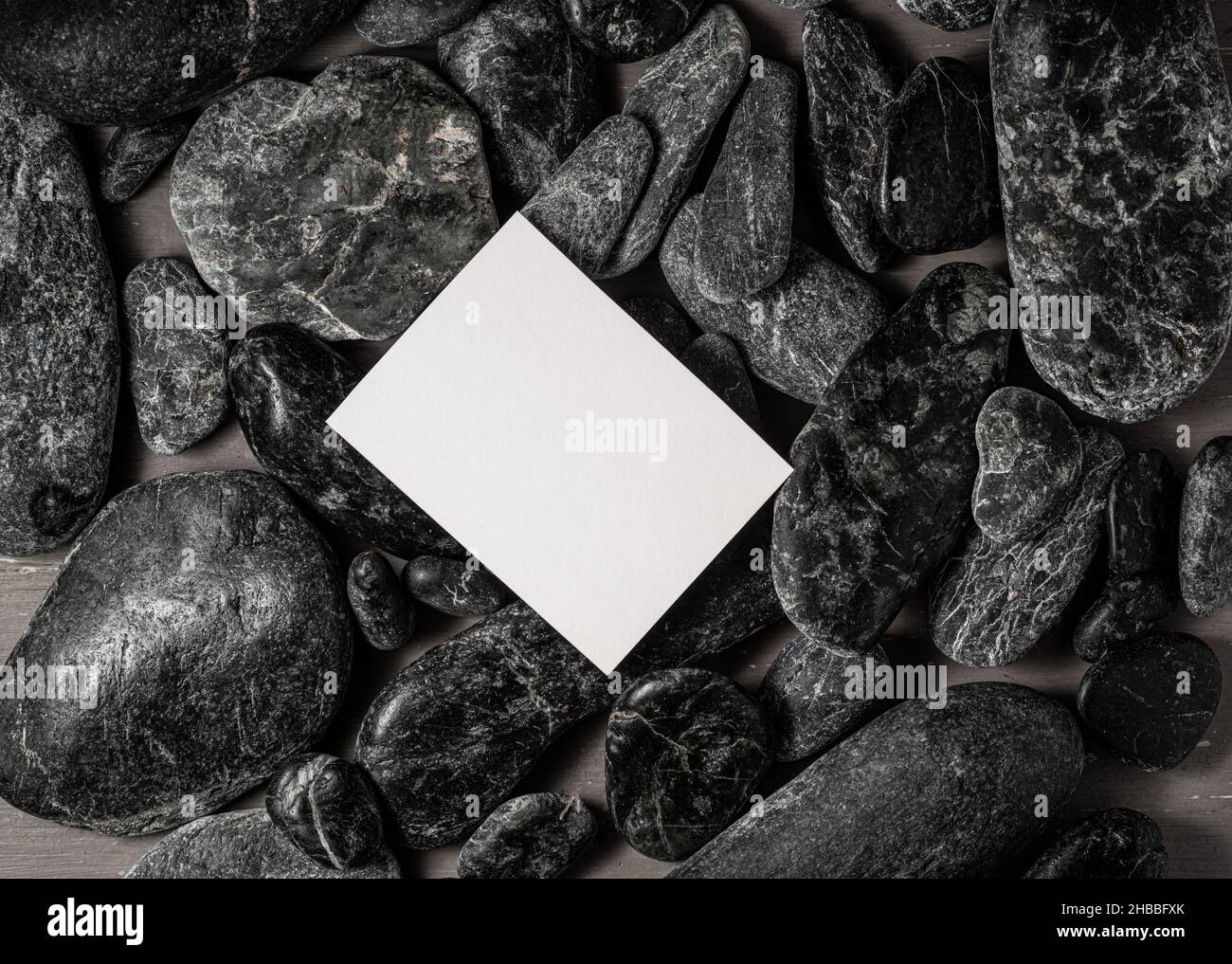 Weiße leere Visitenkarte auf schwarzen Steinen oder Galet, Konzept des Zen Spa oder Sauna Branding. Stockfoto