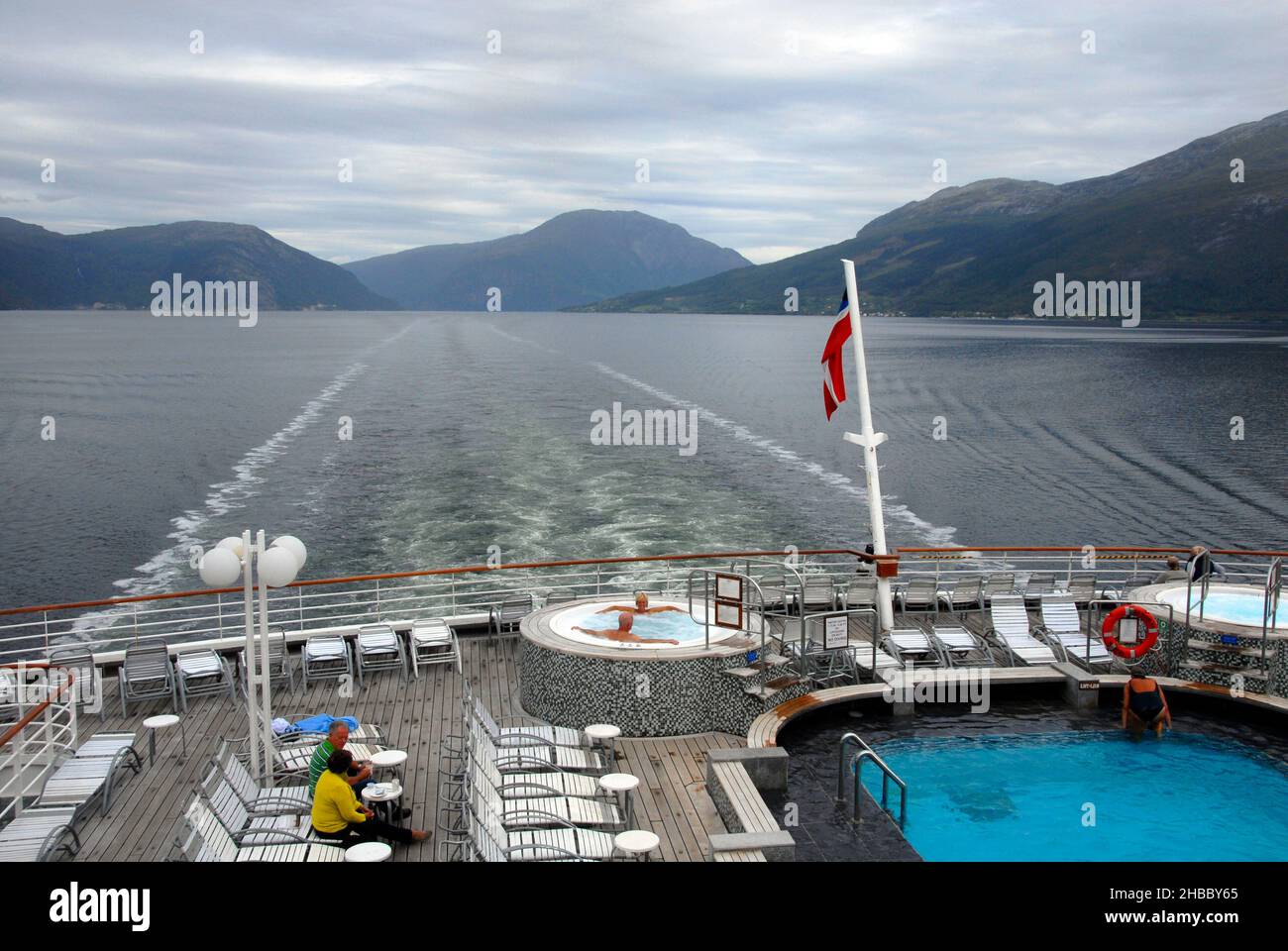 Wachen Sie hinter dem Kreuzschiff im norwegischen Fjord bei bewölktem Wetter auf, nur wenige Passagiere an Deck, aber zwei in einem Whirlpool Stockfoto