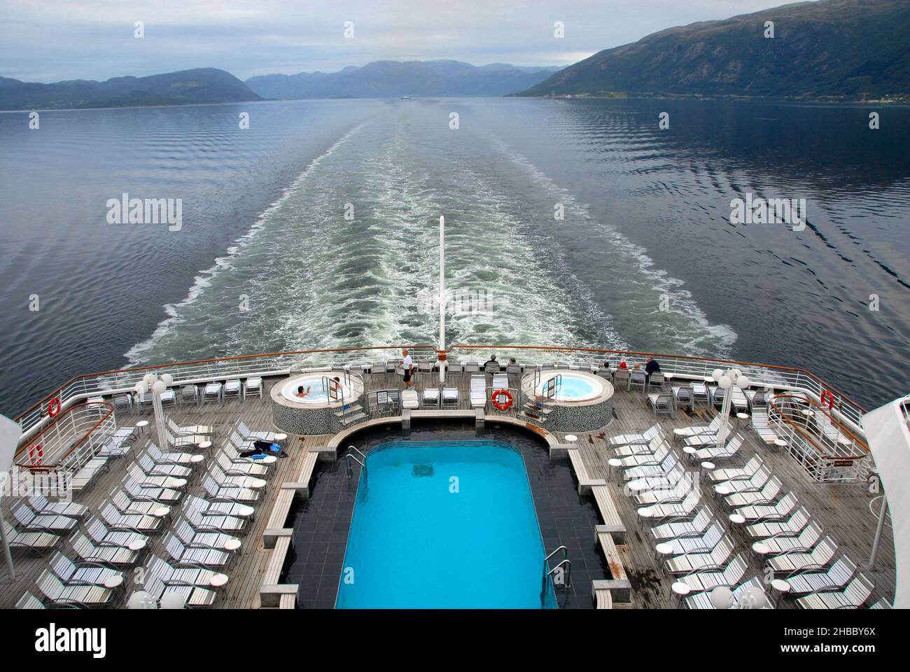 Wachen Sie hinter dem Kreuzschiff im norwegischen Fjord bei bewölktem Wetter auf, nur wenige Passagiere an Deck, aber zwei in einem Whirlpool Stockfoto