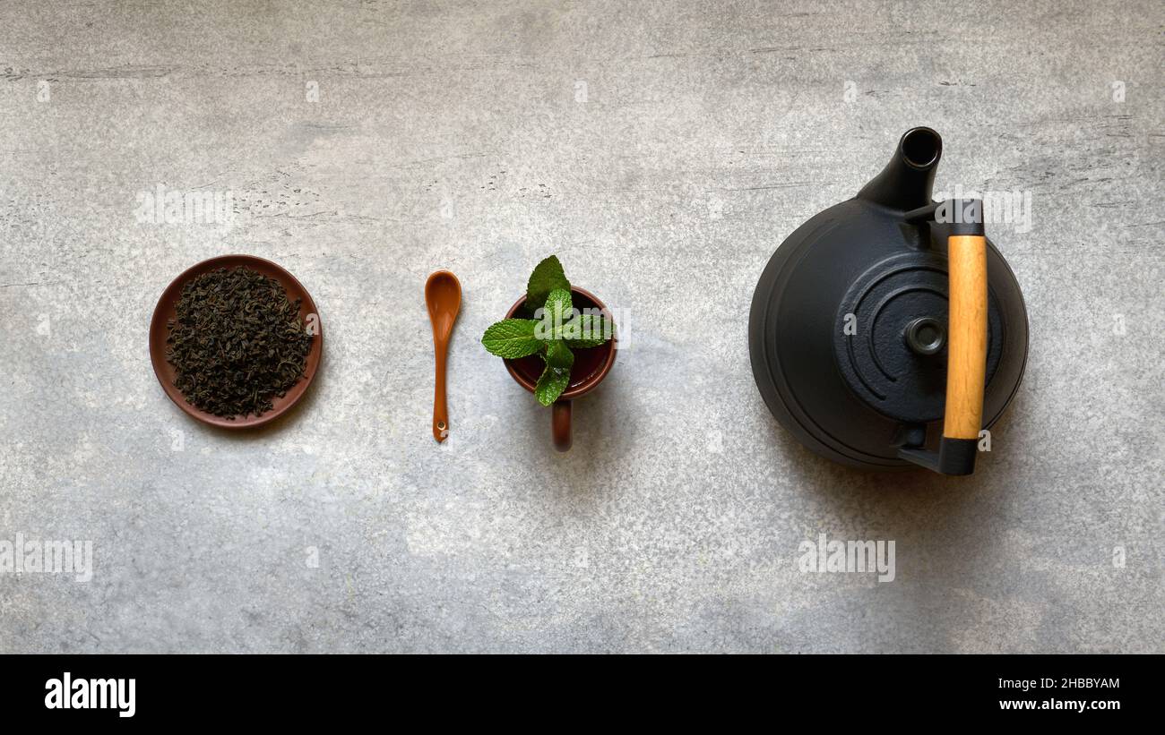 Schwarzer Tee, Teekannen und Teetasse mit Minzblättern, weite Draufsicht auf grauem Hintergrund mit Kopierraum Stockfoto