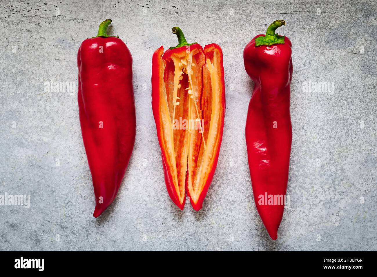 Drei reife rote Paprika-Schoten auf grauem Beton-Hintergrund, Nahaufnahme, kulinarische Zutat Stockfoto