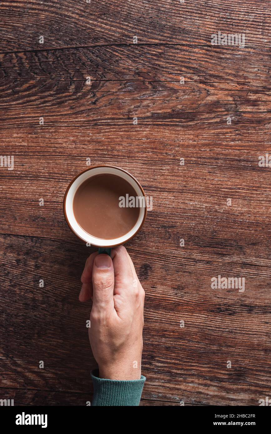 Draufsicht auf anonymen Mann mit Tasse heißen Kaffee mit Milch auf Holztisch platziert Stockfoto