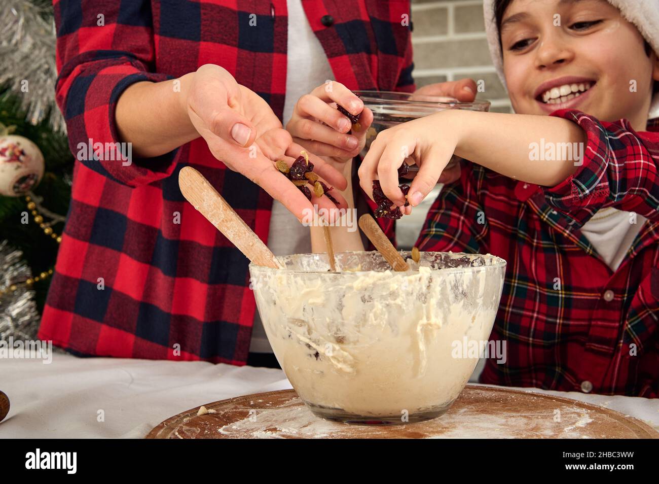 Nahaufnahme der Hände von Mutter und Sohn, die Rosinen in eine Schüssel mit Teig gießen, während sie in der heimischen Küche zusammen kochen Stockfoto
