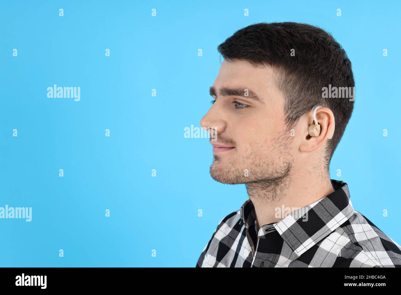 Junger Mann mit Hörgerät auf blauem Hintergrund Stockfoto