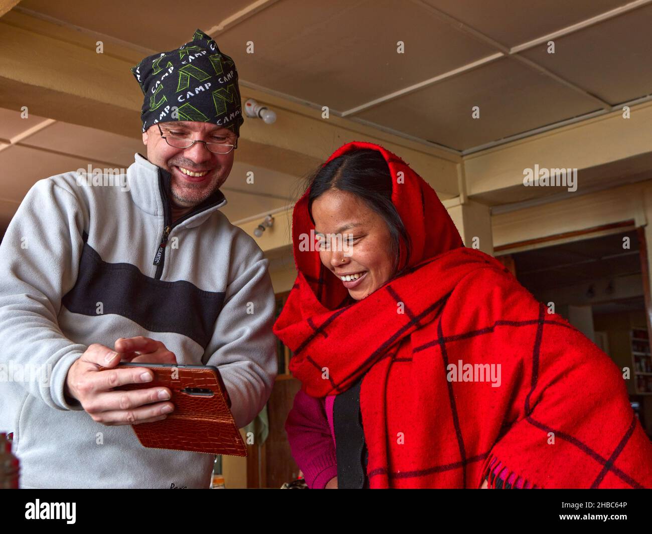 Ein europäischer Mann und ein nepalesisches Mädchen blicken mit einem Lächeln auf ihre Handys. Sie sind beide glücklich. Stockfoto
