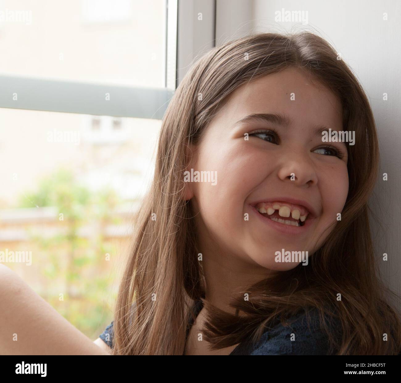 Ein Porträt eines 7-jährigen Mädchens saß auf einem Fensterbrett aus gemischter Rasse, kaukasischer und hispanischer Herkunft Stockfoto