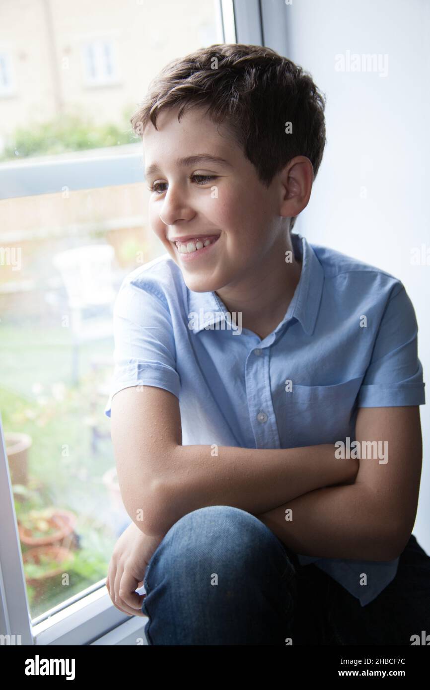 Ein Porträt eines lächelnden Jungen, während er in seinem Haus auf einer Fensterbank saß Stockfoto