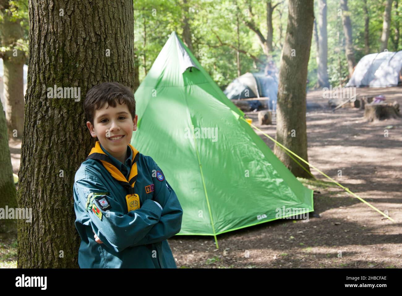 Ein Pfadfinder mit einem Campingplatz hinter ihm auf einer Sommerreise in Großbritannien Stockfoto
